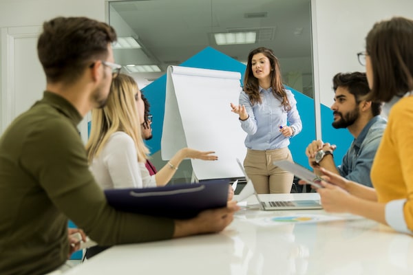 Confident young team leader giving a presentation to a group of young colleagues as they sit grouped by the flip chart in the office Security Awareness Training